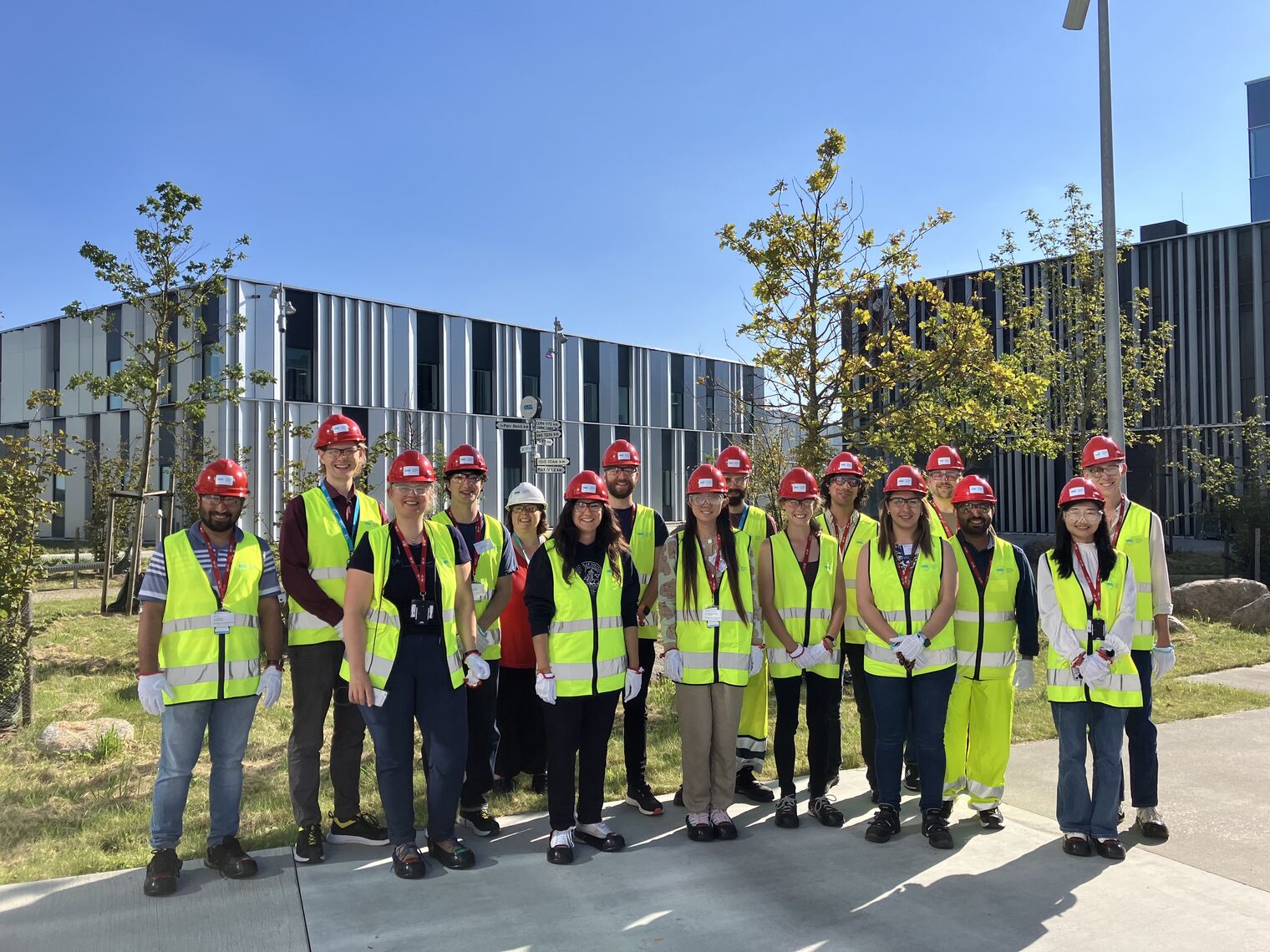 12 people stand in the sunshine wearing red helmets and yellow vests