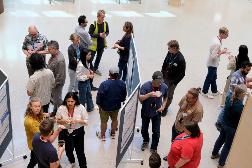 A view from above of a dozen people standing by poster boards engaged in lively conversation