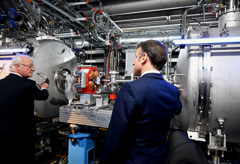 HRH The King of Sweden fixes a small round flange to a cryomodule on the left, while President Macron on his right fits another, indicating the final installation of the Spoke Cryomodules