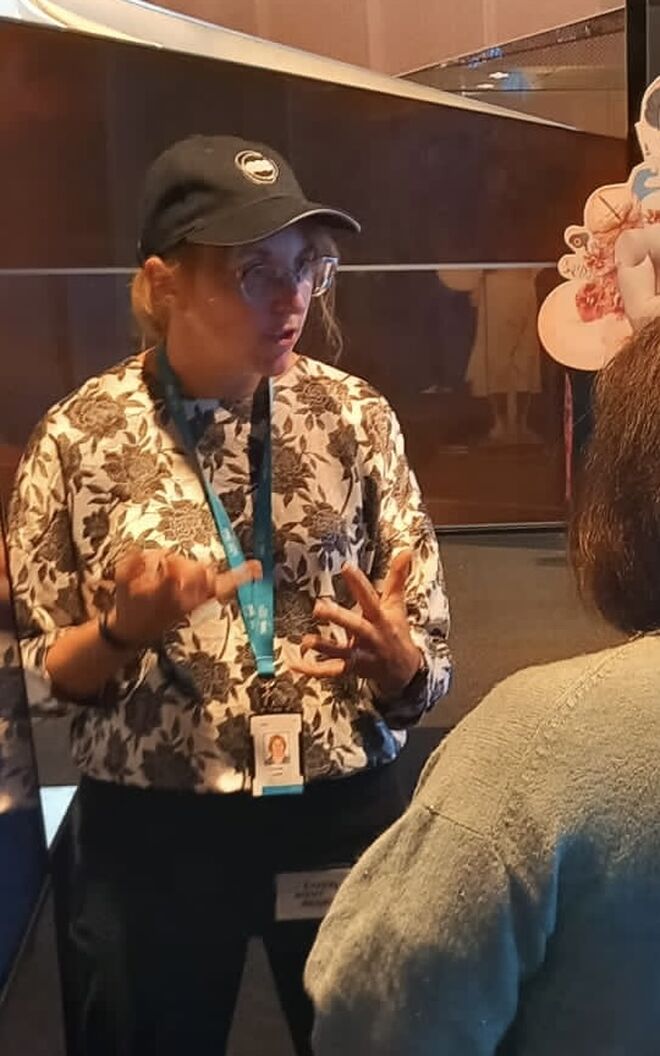 ESS staff member, wearing a branded hat, talks animatedly with a lady who has her back to the camera