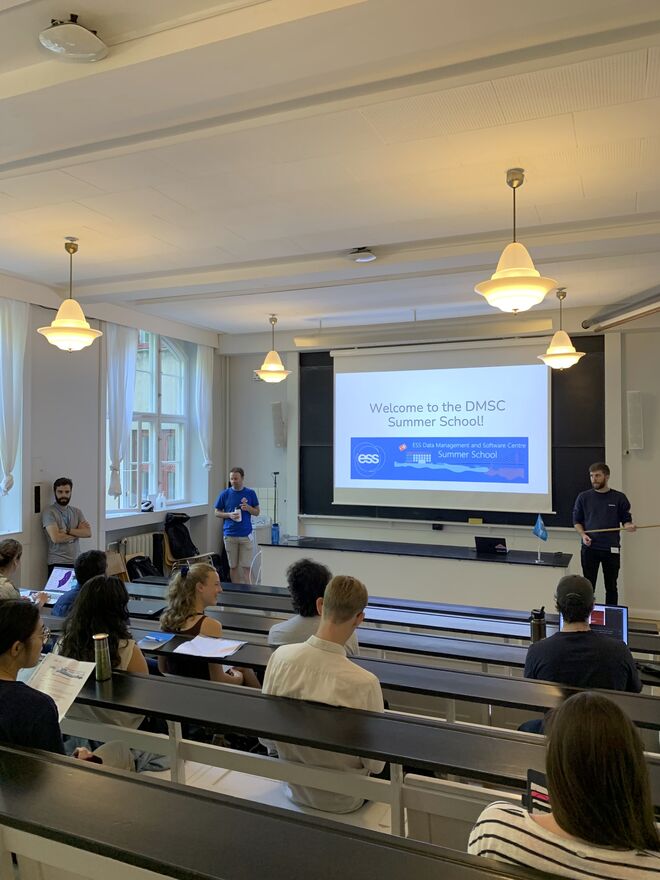 Student sit in a cosy tiered lecture room facing a screen that reads 'Welcome to the DMSC Summer School'